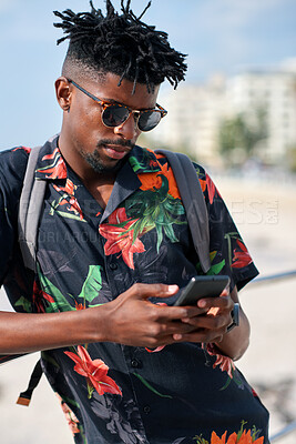 Buy stock photo Phone, travel and black man by beach on holiday for texting, social media or contact on mobile app. Tech, promenade and male person on cellphone for blog on vacation tips on seaside weekend trip.