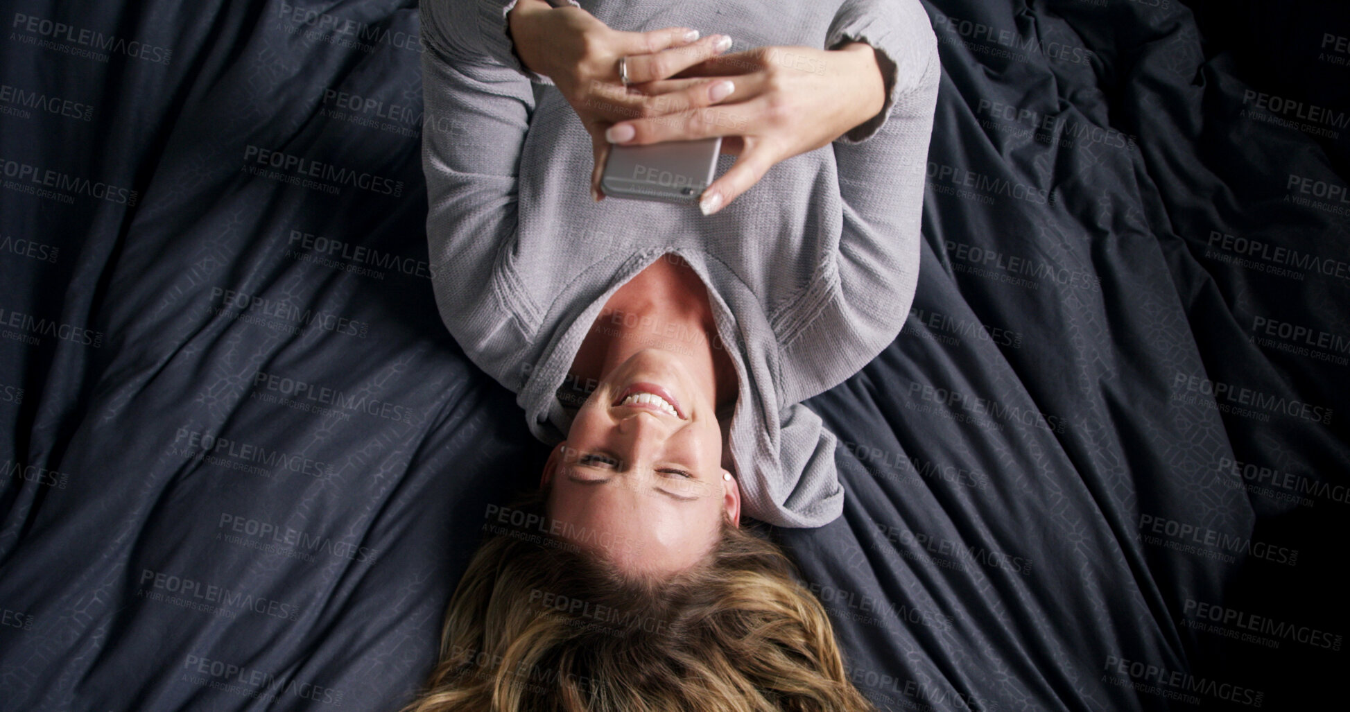 Buy stock photo Above, smile and woman in bed with phone, text or reading funny meme on social media in home. Laugh, relax or person in bedroom on mobile app for typing message, morning notification or communication