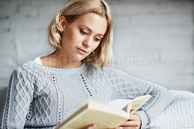 Buy stock photo A candid shot of a young woman reading a book while sitting on the couch 