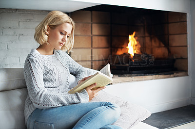 Buy stock photo Cropped shot of a beautiful young woman curling up on the couch with a novel 