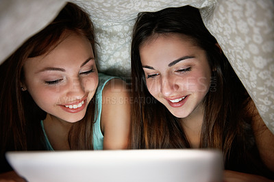 Buy stock photo Shot of two teenage girls under a blanket looking at a digital tablet
