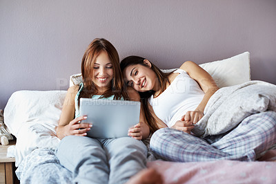 Buy stock photo Shot of two teenage girls at a slumber party sitting on a bed looking at a digital tablet