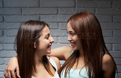 Buy stock photo Shot of two teenage girl friends smiling at each other in front of a brick backround