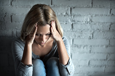 Buy stock photo A pretty young blonde woman sitting down while looking severely depressed