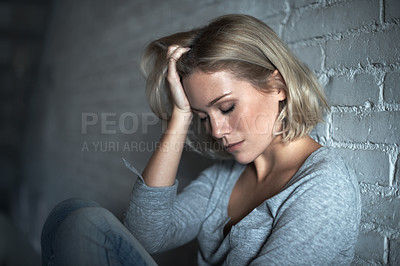 Buy stock photo A pretty young blonde woman sitting down while looking severely depressed
