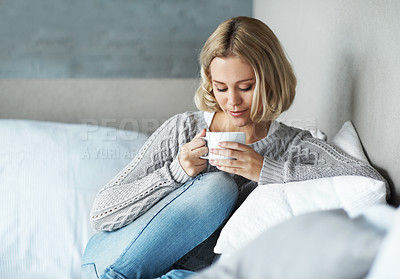 Buy stock photo A young blonde woman looking down as she enjoys a cup of coffee at home