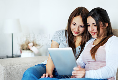 Buy stock photo Two teenage girls sharing a digital tablet while sitting on the couch at home