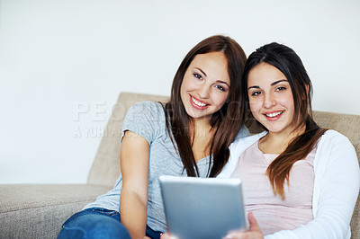 Buy stock photo Portrait of two teenage girls sharing a digital tablet while sitting on the sofa at home