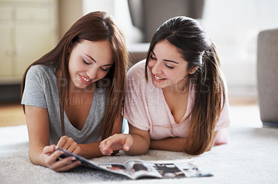 Buy stock photo Two teenage girls lying on the floor while paging through a magazine