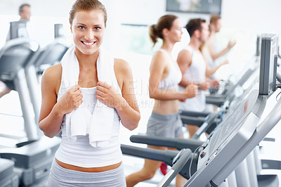 Buy stock photo Healthy young woman standing alongside a row of treadmills at the gym