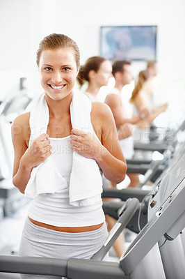 Buy stock photo Smiling young woman standing alongside a row of treadmills at the gym