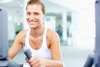 Buy stock photo Young woman using an exercise bicycle while listening to music - portrait