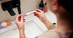 Hands, pregnancy test and results in bathroom, home and check for fertility with screen in morning. Asian person, monitor or stick for outcome, IVF and sample at basin with waiting in apartment