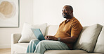 Laptop, relax and thinking with black man on sofa in home living room for break or browsing. Computer, planning and smile with mature person in apartment for calendar, research or weekend schedule