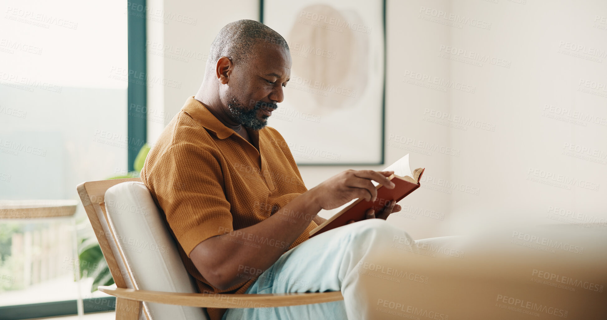 Buy stock photo Reading, relax and weekend with black man on chair in home living room for break or hobby. Happy, novel and story book with mature person in apartment for literature, me time or tale of fiction