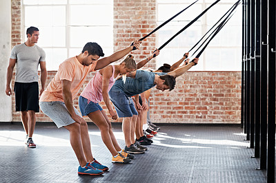 Buy stock photo Shot of a group of people using resistance bands in a crossfit class while an instructor looks on