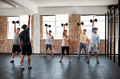 Buy stock photo Shot of a group of people lifting dumbbells in a fitness class