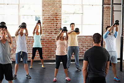 Buy stock photo Shot of a group of people lifting kettlebells in a fitness class