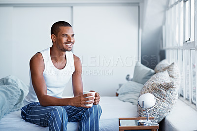 Buy stock photo Cropped shot of a young man drinking coffee while sittng on his bed