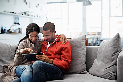 Buy stock photo Cropped shot of a young couple using their tablet while sitting on the sofa at home