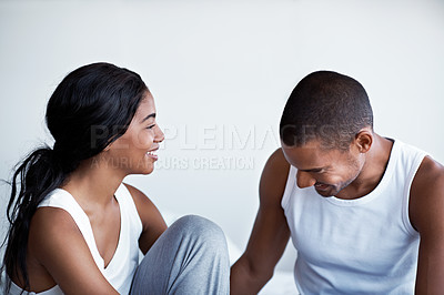 Buy stock photo Shot of young couple talking together while sitting on their bed