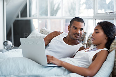 Buy stock photo Shot of a young couple lying in bed using a laptop