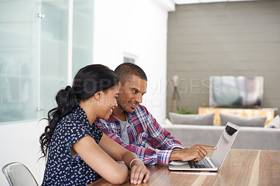 Buy stock photo Shot of a young couple sitting at their dining table using a latpop