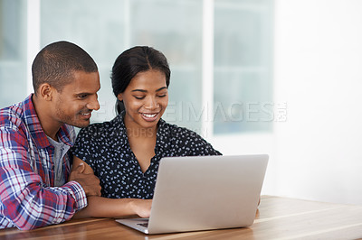 Buy stock photo Shot of a young couple sitting at their dining table using a latpop