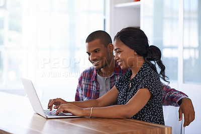 Buy stock photo Shot of a young couple sitting at their dining table using a latpop
