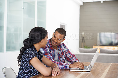 Buy stock photo Shot of a young couple sitting at their dining table using a latpop