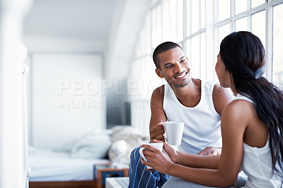 Buy stock photo Shot of a young couple talking together and drinking coffee while sitting in their bedroom