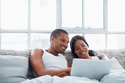Buy stock photo Shot of a young couple lying in bed together using a laptop