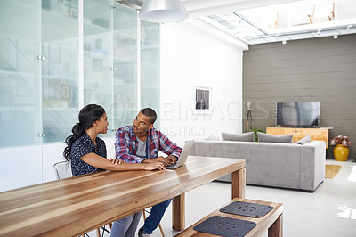 Buy stock photo Shot of a young couple sitting together at their kitchen table using a laptop