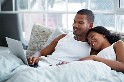 Buy stock photo Shot of a young couple lying in bed using a laptop