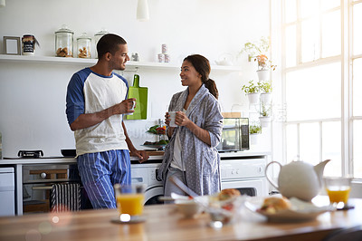 Buy stock photo Shot of a young couple talking together and drinking coffee in their kitchen in the morning