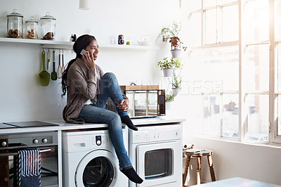 Buy stock photo Shot of a young woman sitting on her kitchen counter talking on the phone