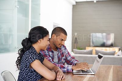 Buy stock photo Shot of a young couple sitting at their dining table using a latpop