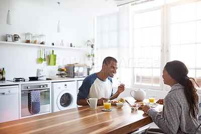 Buy stock photo Shot of a young couple eating breakfast together in their kitchen