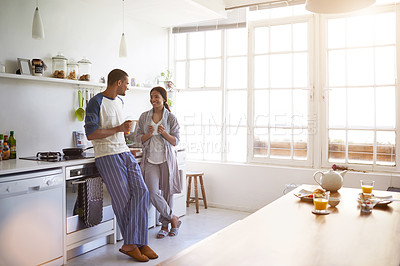 Buy stock photo Shot of a young couple talking together and drinking coffee in their kitchen in the morning