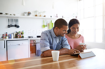 Buy stock photo Shot of a young couple drinking coffee and using their tablet in the kitchen