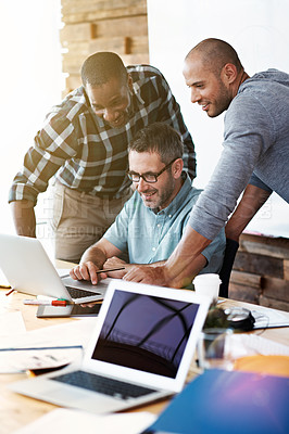 Buy stock photo Shot of three colleagues standing in an office talking together over a laptop