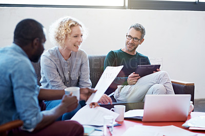 Buy stock photo Shot of a group of smiling colleagues talking discussing paperwork while sitting on a sofa in a modern office