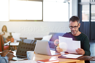 Buy stock photo Shot of a mature businessman looking over some paperwork in the office