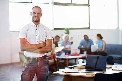 Buy stock photo Shot of a handsome young businessman standing with his arms folded in the office