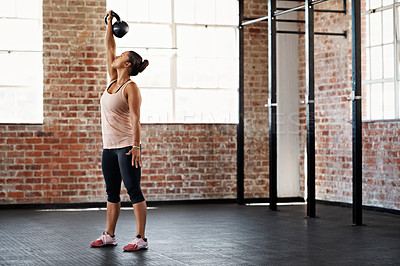 Buy stock photo Full length shot of a young woman doing a workout with a kettlebell in a gym