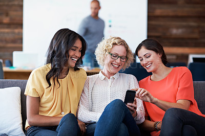 Buy stock photo Shot of three work colleagues laughing together while looking at a cellphone