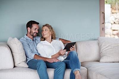 Buy stock photo Cropped shot of a couple using a tablet while relaxing on the sofa