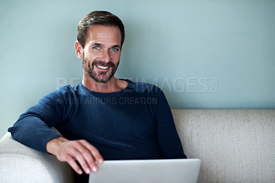 Buy stock photo Cropped portrait of a handsome man using his laptop while sitting on the living room sofa