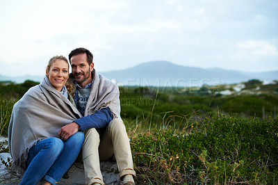 Buy stock photo Cropped portrait of an affectionate couple wrapped in a blanket while sitting outdoors