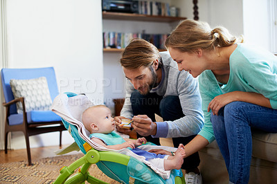 Buy stock photo Shot of a young couple feeding their baby at home